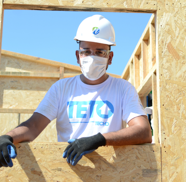 Trabalhador da Novolar utilizando equipamentos de proteção em construção emergencial, da ONG TETO representando responsabilidade social e ambiental.
