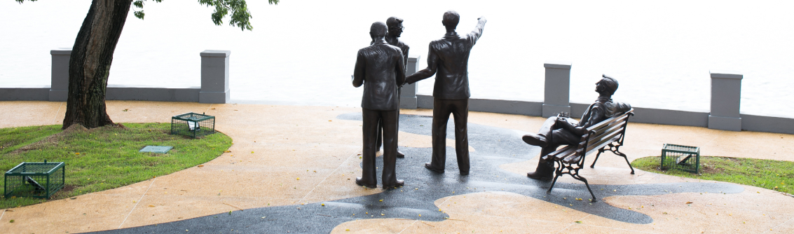 Restauração de praça, com escultura de figuras históricas, representando a preservação de um patrimônio cultural.